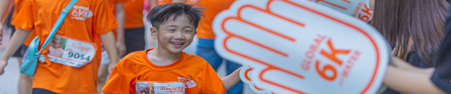 글로벌 6K 행사장에서 주황색 티셔츠를 입은 아이 참가자가 환하게 웃으며 걷고 있다.
