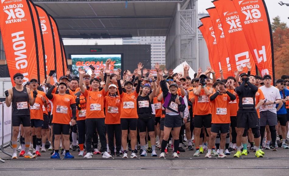 출발선 앞에서 수많은 러너들이 주황색 티셔츠를 입고 손을 들며 글로벌 6K 마라톤 시작을 기다리고 있다.